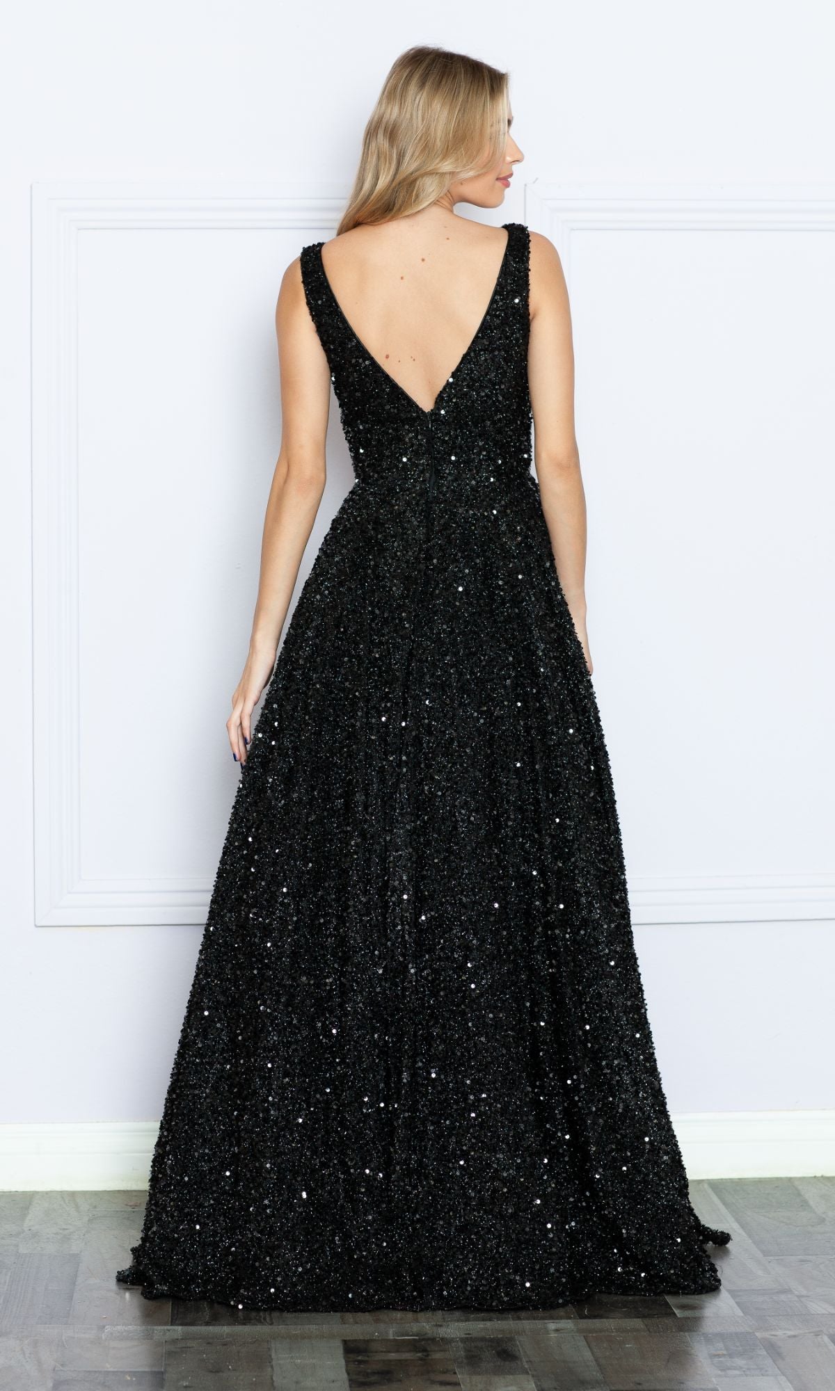A woman faces away, wearing the Long Black Sequin A-Line Prom Dress 9168, a floor-length, sleeveless gown with shimmering sequins and a striking deep V-back.